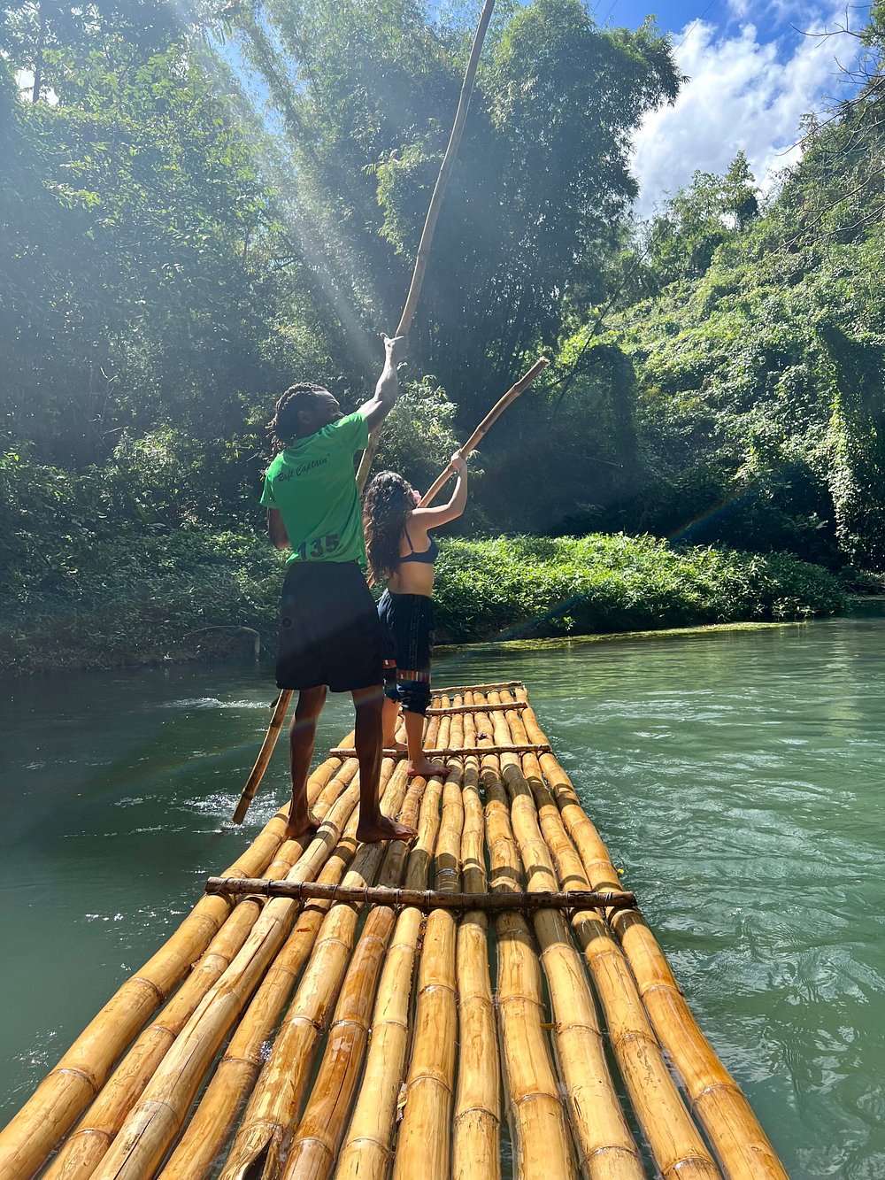 Bamboo rafts glide through the lush waters of the Martha Brae River in Jamaica, surrounded by tropical foliage and vibrant flowers, offering a peaceful outdoor adventure.