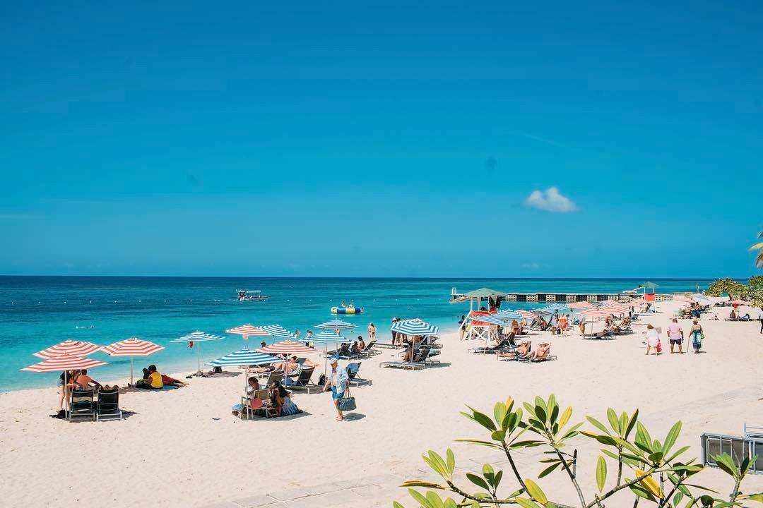 Tourists lounging under umbrellas on the serene Seven Mile Beach.