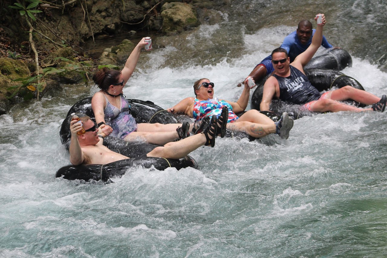 Group of people floating on inner tubes down the gentle rapids of White River, surrounded by lush jungle.