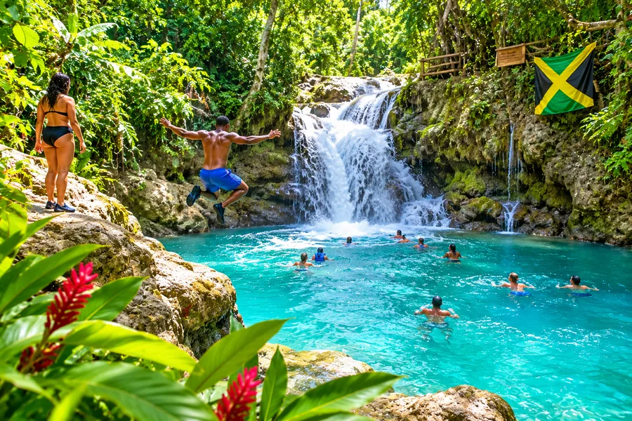 Visitors swimming beneath a tropical waterfall at Blue Hole in Ocho Rios, Jamaica